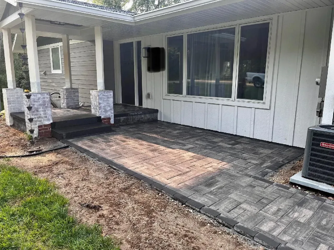 Front exterior of a house with a paved porch and walkway. Gray and brown pavers are used. 