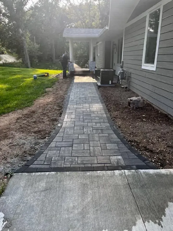 A brick walkway leads from a concrete sidewalk to a house.