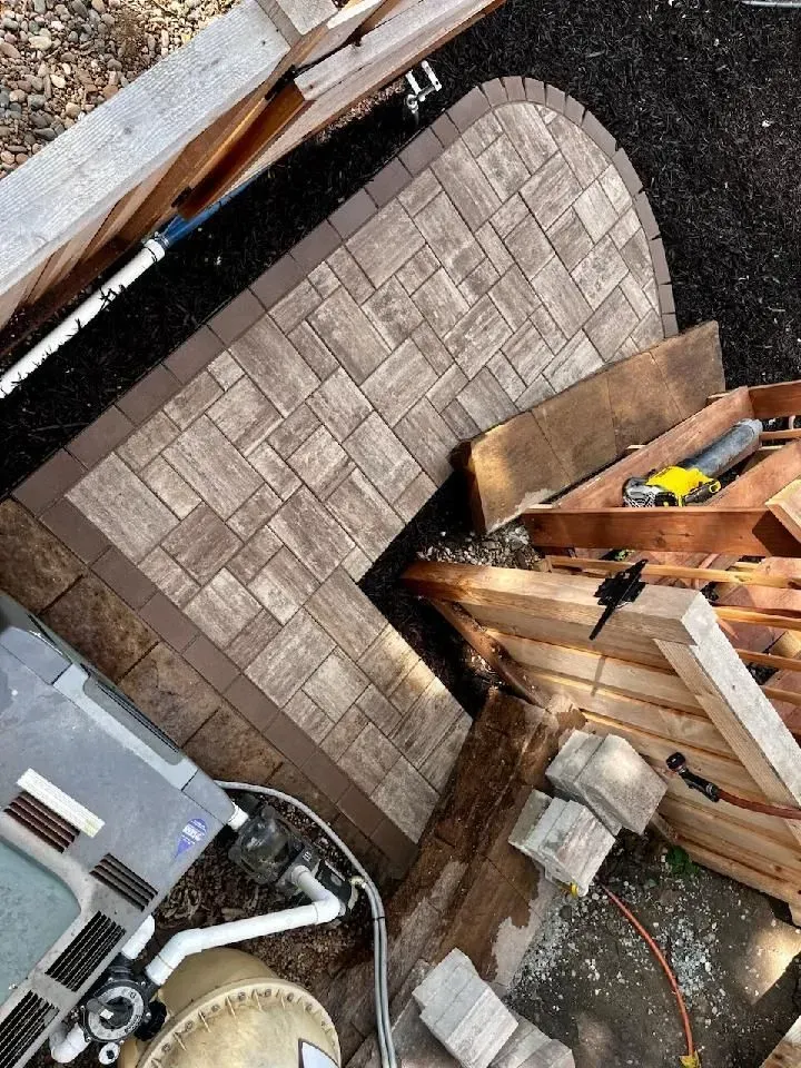 Overhead view of a small patio with brown pavers, a curved edge, and a dark brown border. 
