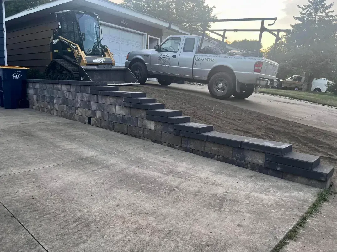A silver pickup truck parked on a concrete driveway next to a retaining wall with steps. 