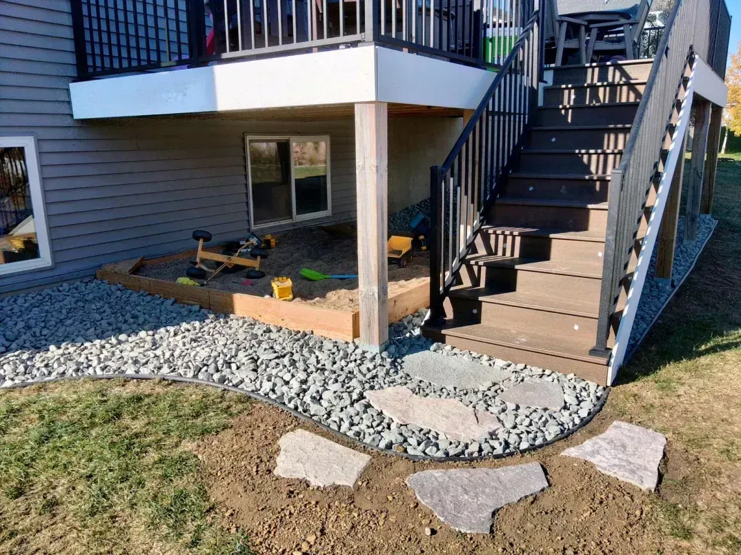 Exterior view of a deck with stairs, gravel border, and stepping stones on a grassy yard.