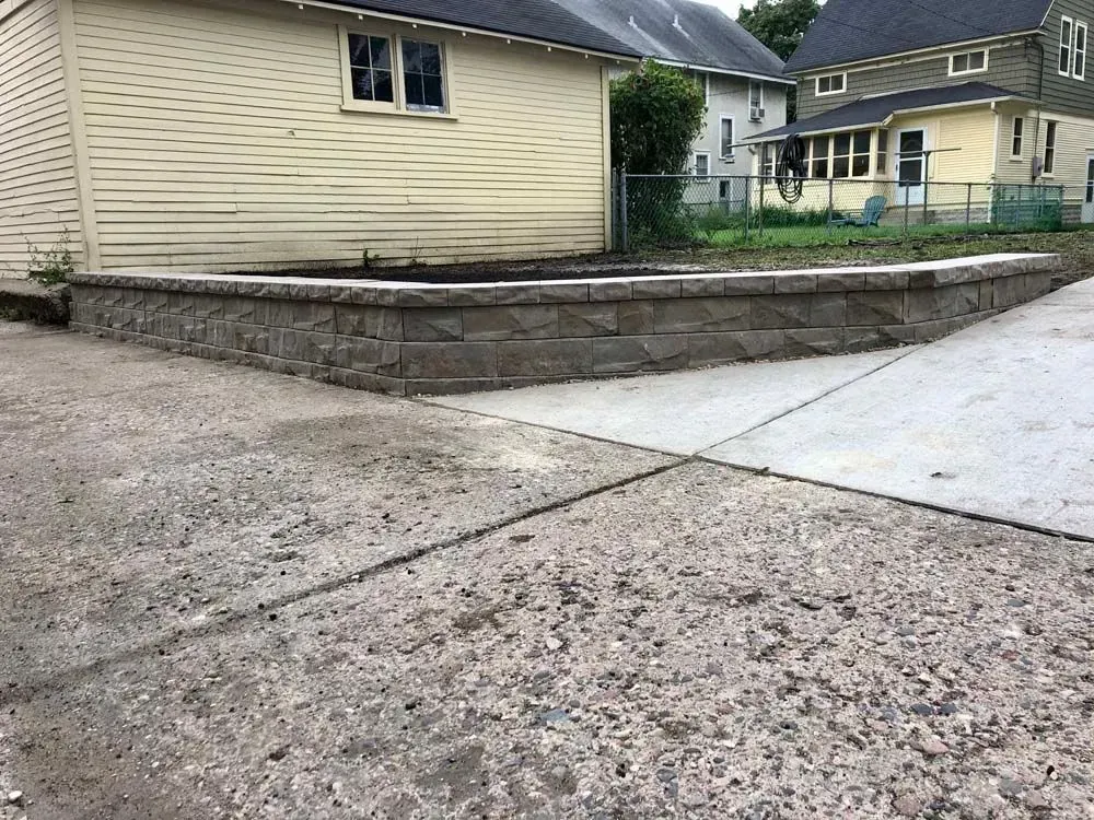 Concrete retaining wall beside a driveway; houses in the background.
