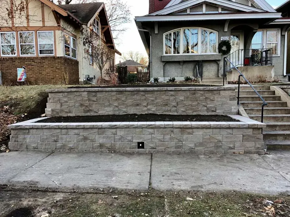 Stone retaining wall with a planter box in front of a house. Steps lead up to the house.