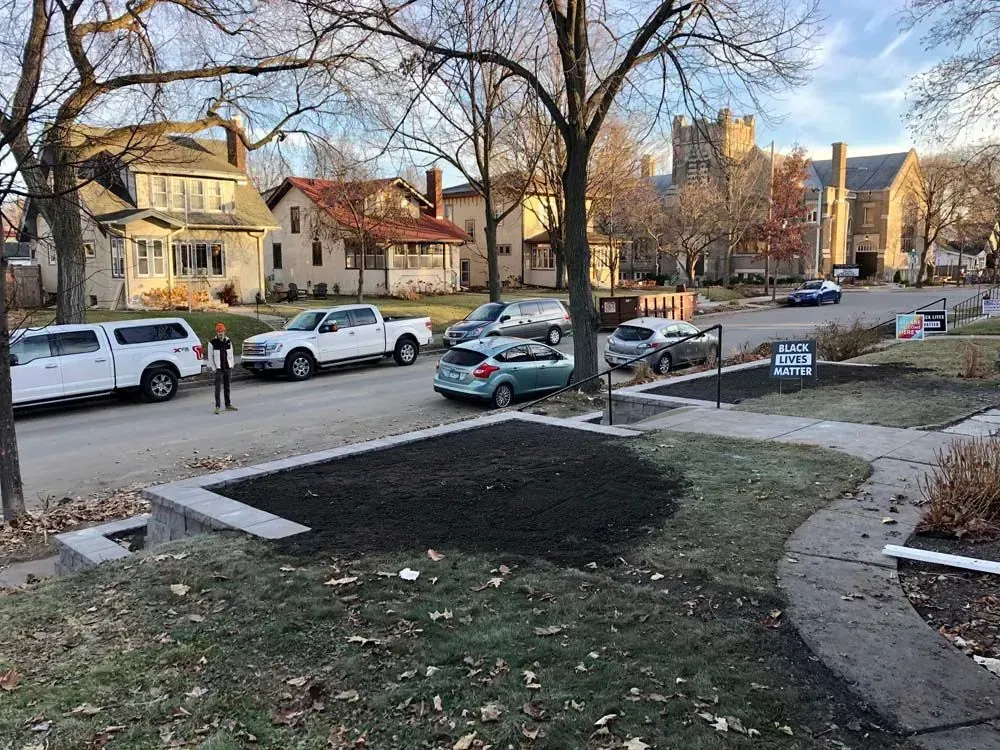 A residential street scene with parked cars, houses, trees, and a church building. Early morning light.