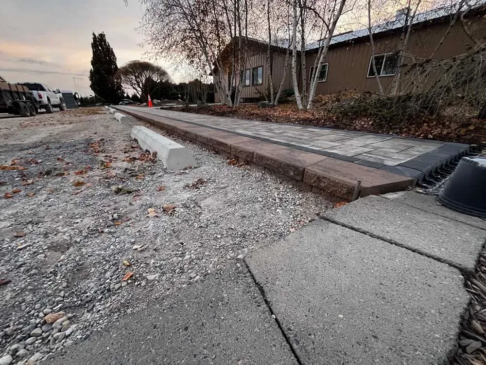 Construction site with a newly paved walkway featuring brick borders next to a gravel area.  