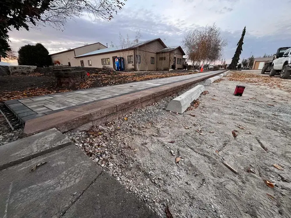 A construction site with a concrete pathway in front of a low building. Debris & equipment are scattered around the pathway.