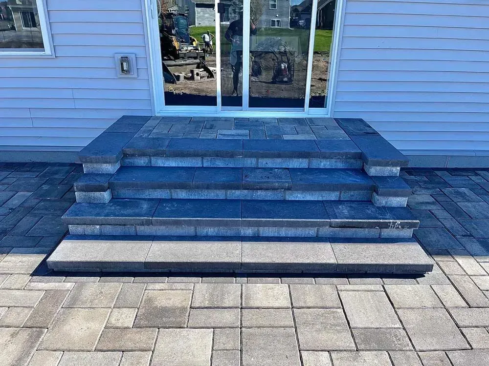 A gray stone staircase leading up to a sliding glass door. The steps are framed by matching stone and sit on a paved patio.