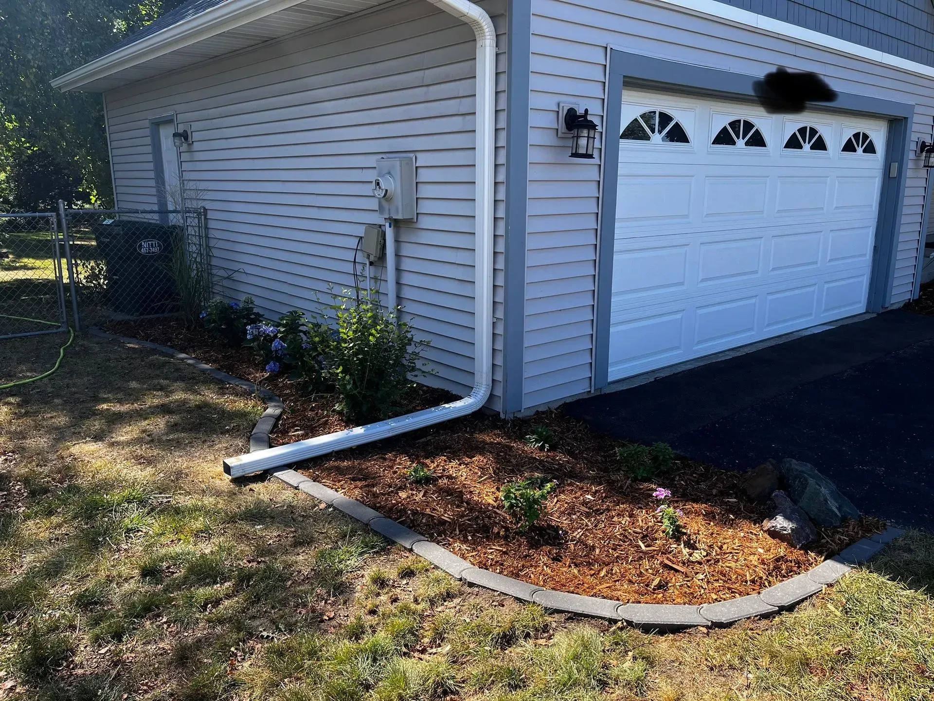 A gray garage with a white door and a flower bed with brown mulch and a concrete border.