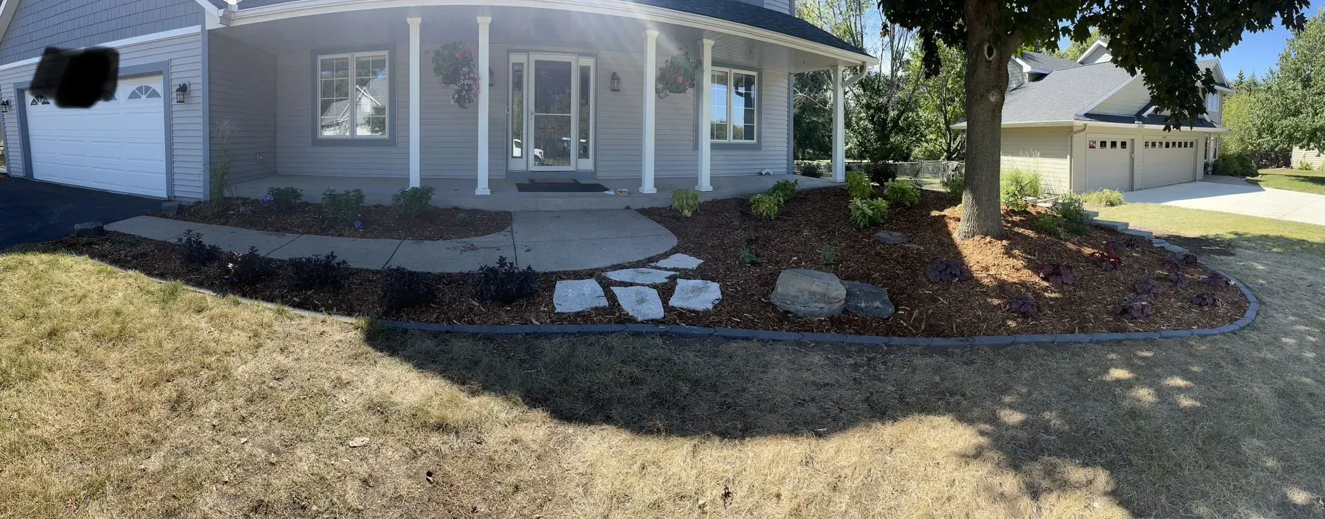 Exterior view of a gray house with a curved porch, landscaping, and a walkway with stone steps in front.