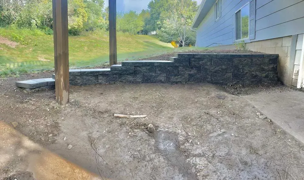 A leveled dirt yard in front of a house with a retaining wall, stairs, and a covered porch.