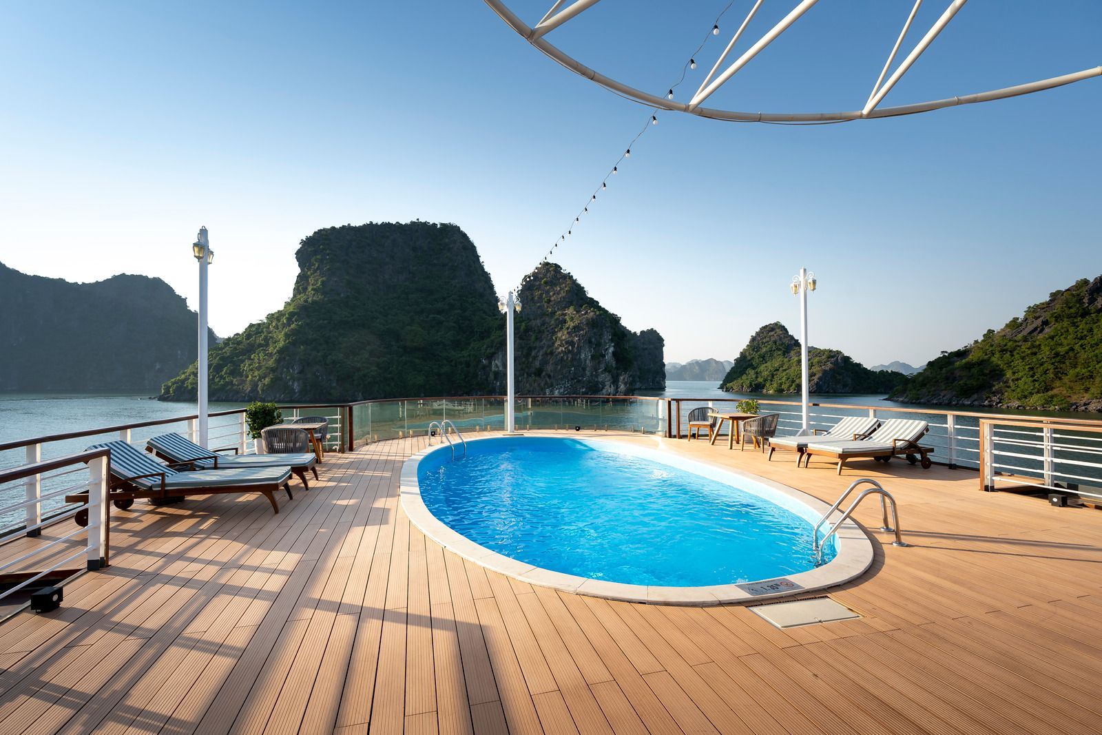 Swimming pool on a wooden deck with a bay and lush green islands in the background under a clear blue sky.