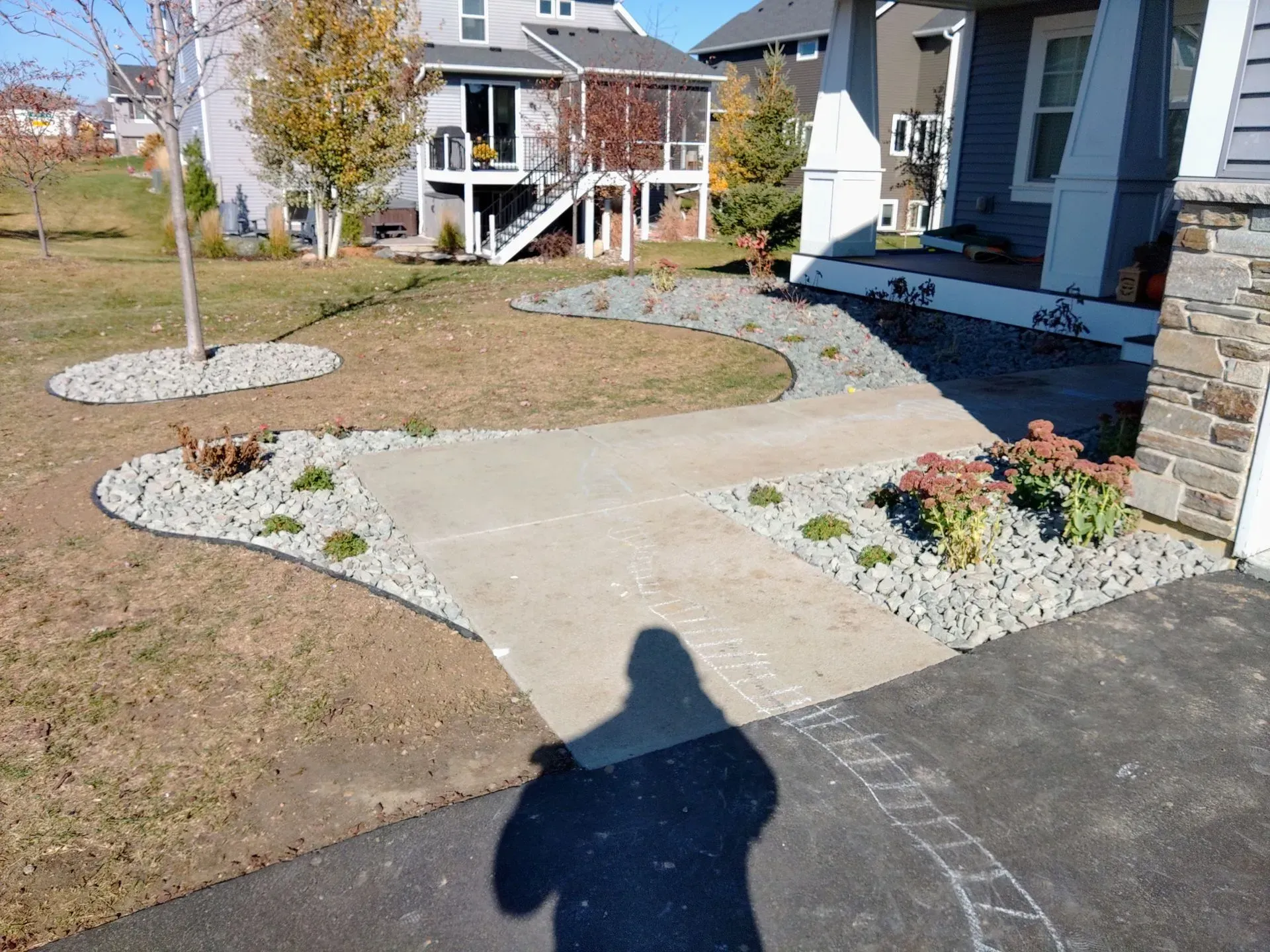 Concrete walkway leading to a house with a gray exterior and stone accents; landscaping with rocks and plants.