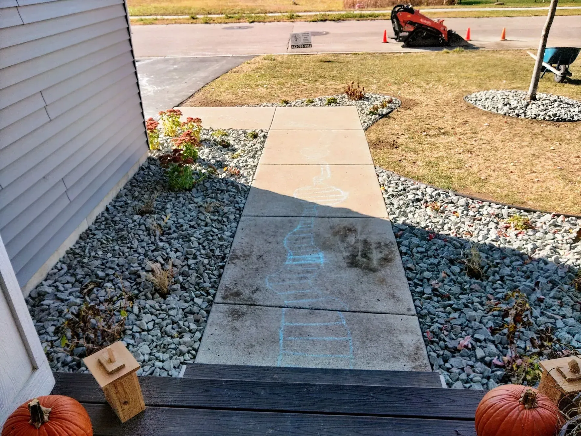 A walkway leading to a house's front door, flanked by rocks and small plants. Pumpkins and decorations are on the steps.
