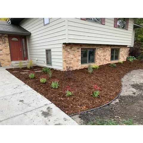 House exterior with beige siding, brick accents, and a freshly mulched garden bed with new plants 