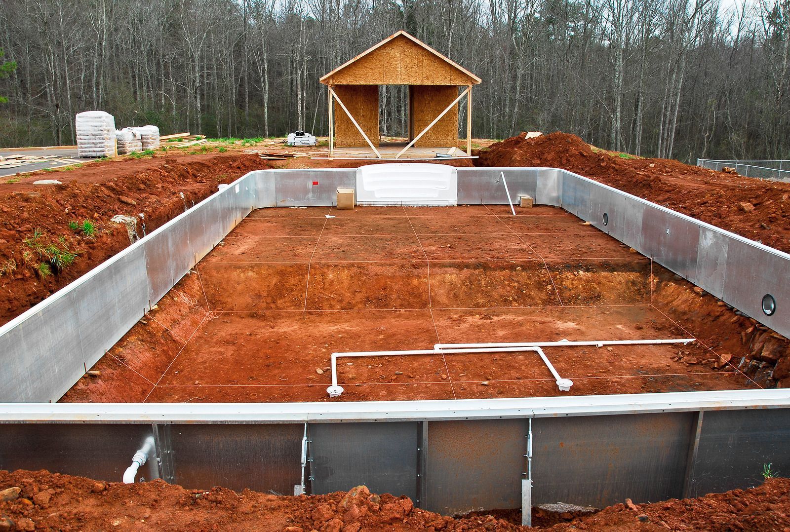 Pool under construction with a rectangular shape, metal sides, & plumbing visible. A wooden structure sits in the background.