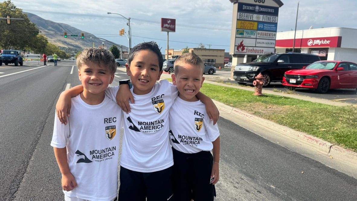 Baseball player sliding into home plate, catcher in front. Blue and gold uniforms, action shot.