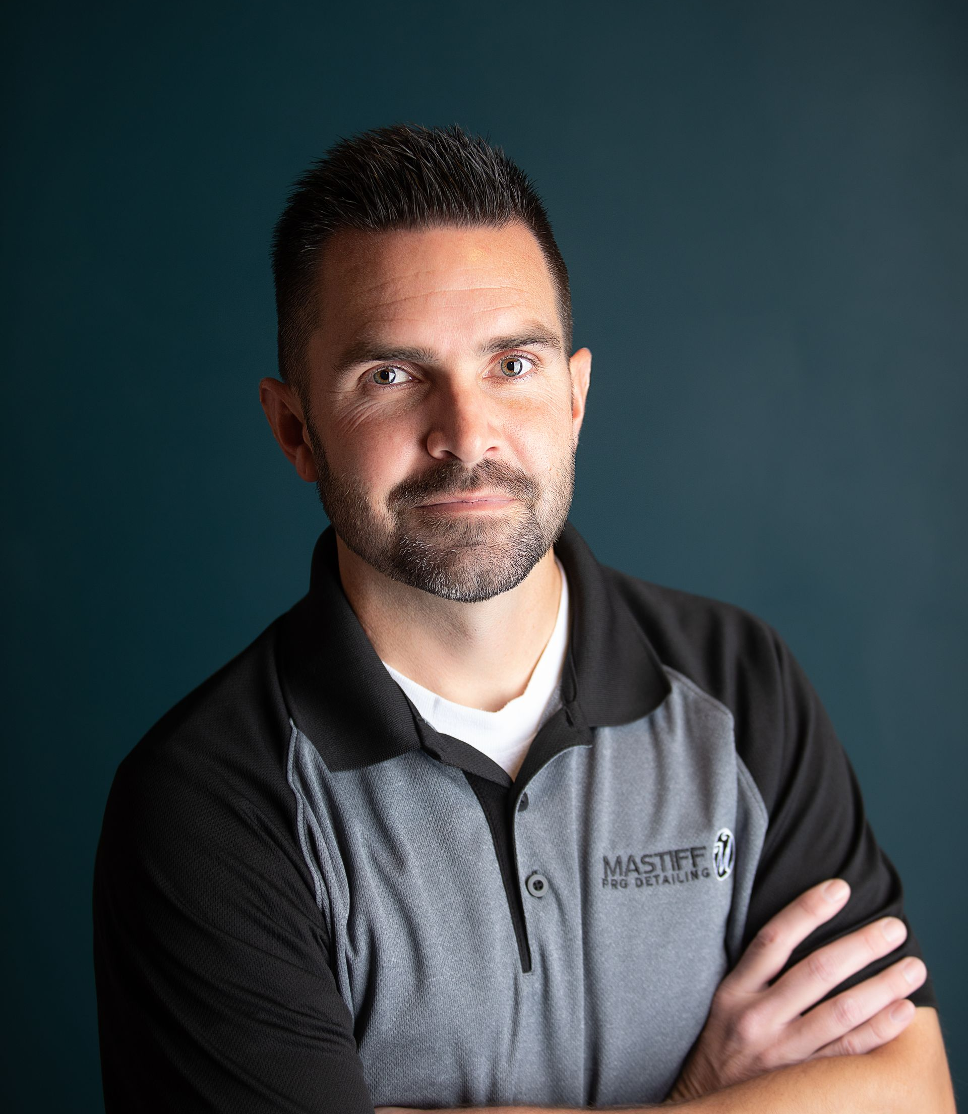 Man in green polo stands on a football field, arms crossed, stadium in background.