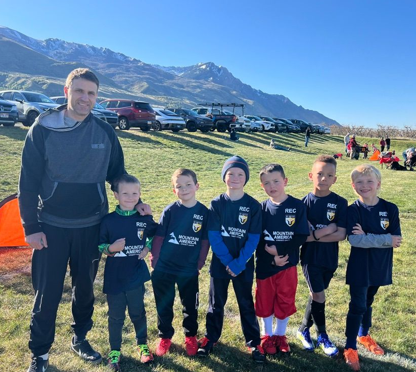 Baseball player sliding into home plate, catcher in front. Blue and gold uniforms, action shot.