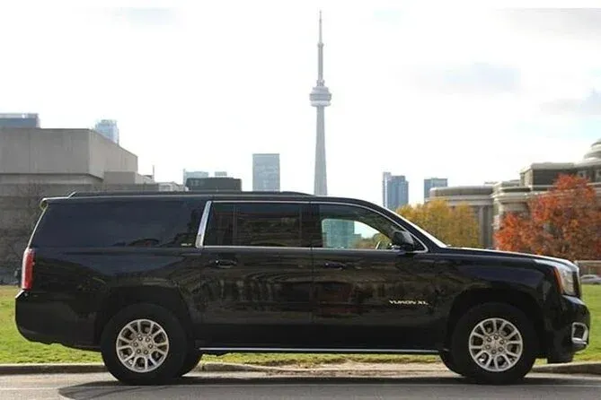 A black suv is parked on the side of the road in front of a city skyline.