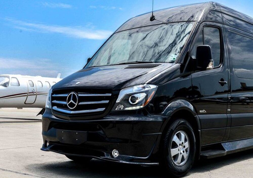 A black mercedes van is parked in front of a private jet.