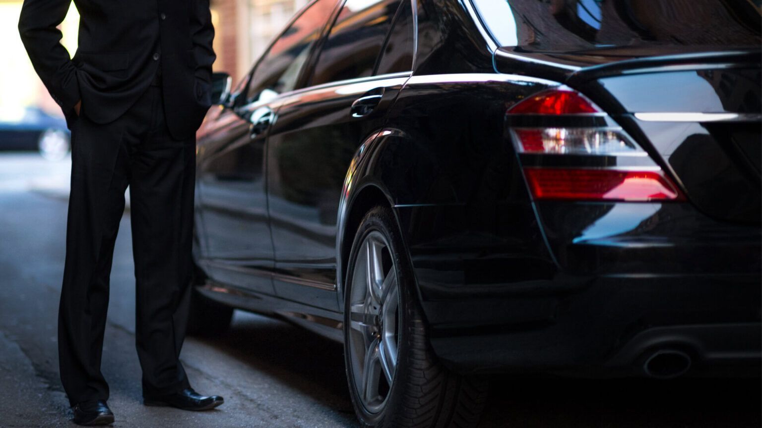 A man in a suit is standing next to a black car.