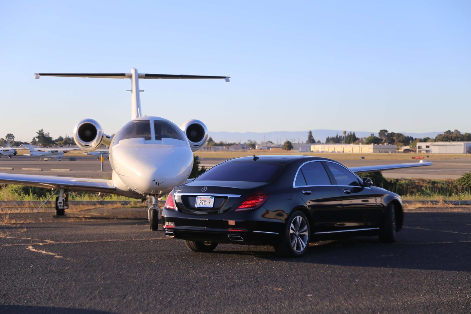 A car is parked next to a private jet on a runway.