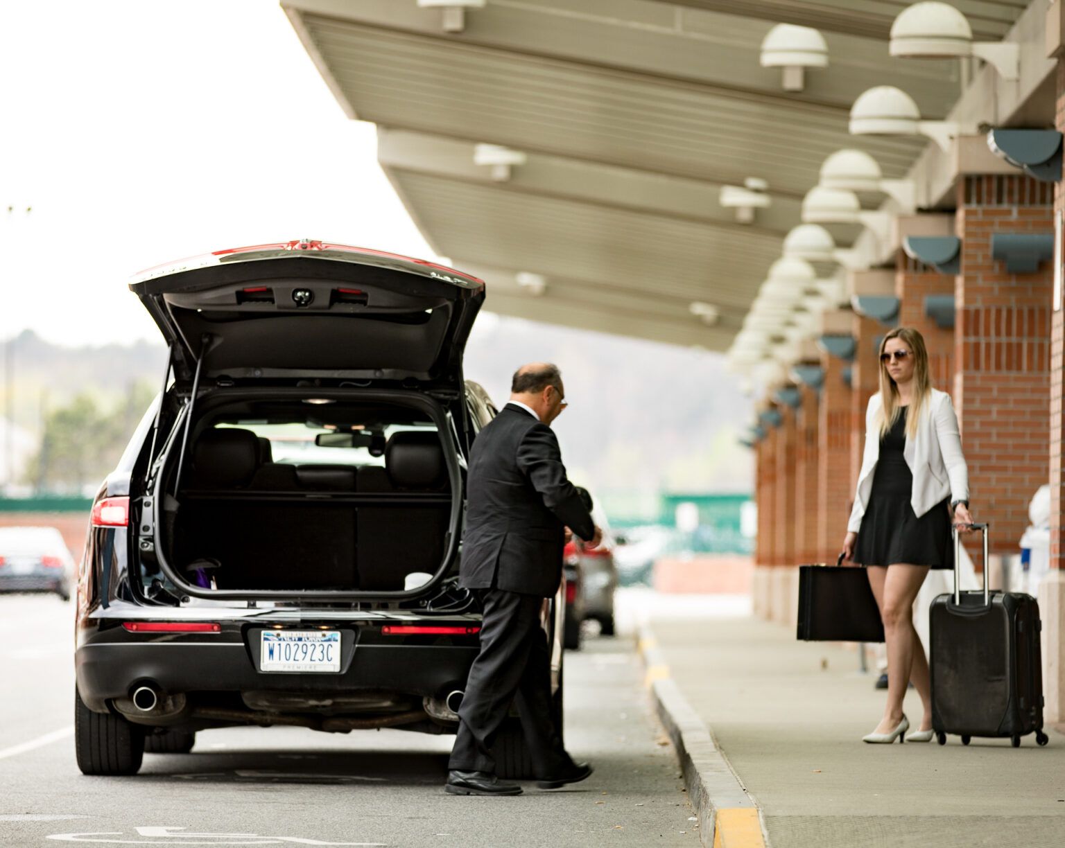 A man is loading luggage into the back of a car while a woman looks on.