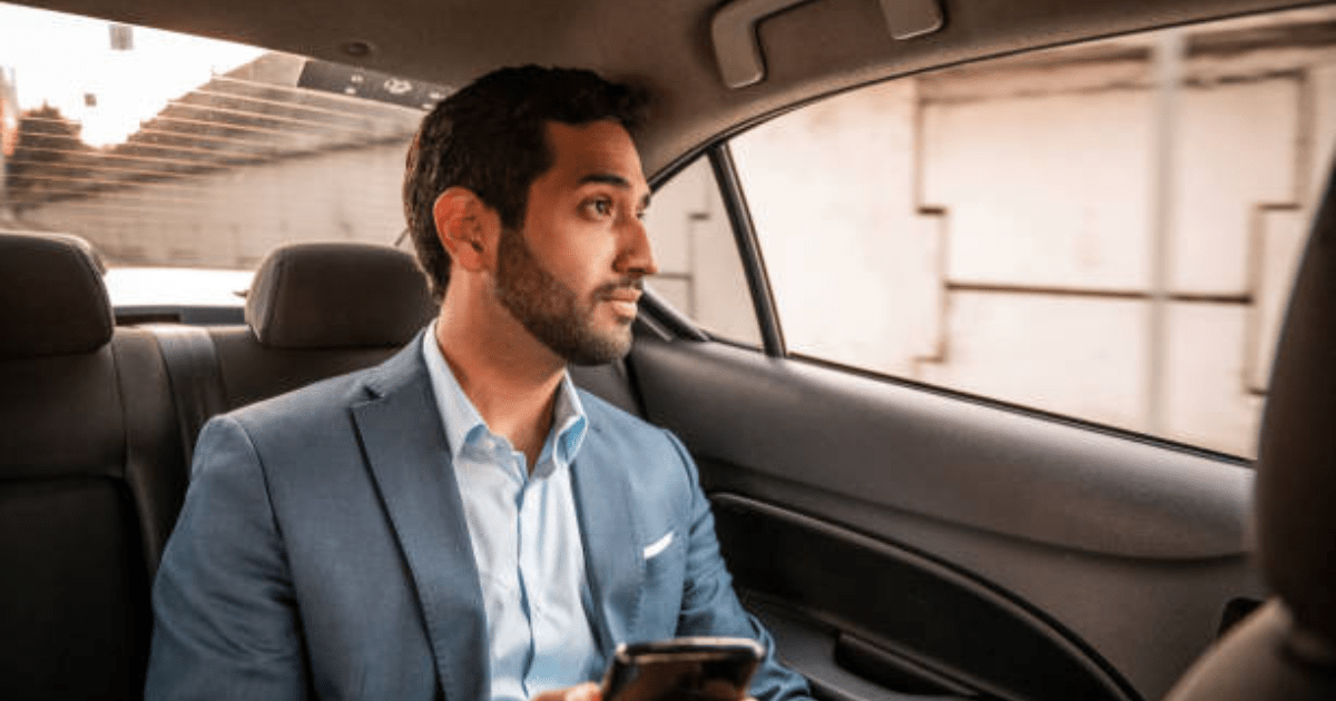 A man in a suit is sitting in the back seat of a car holding a cell phone.