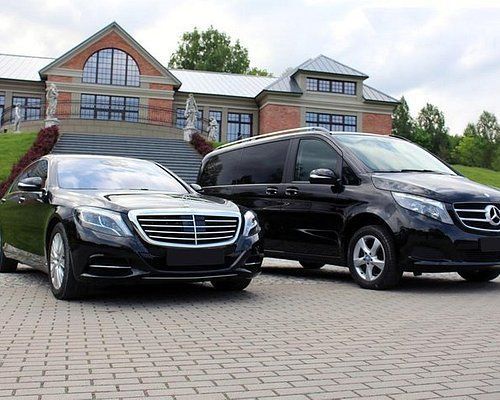 Two black cars are parked in front of a large building.