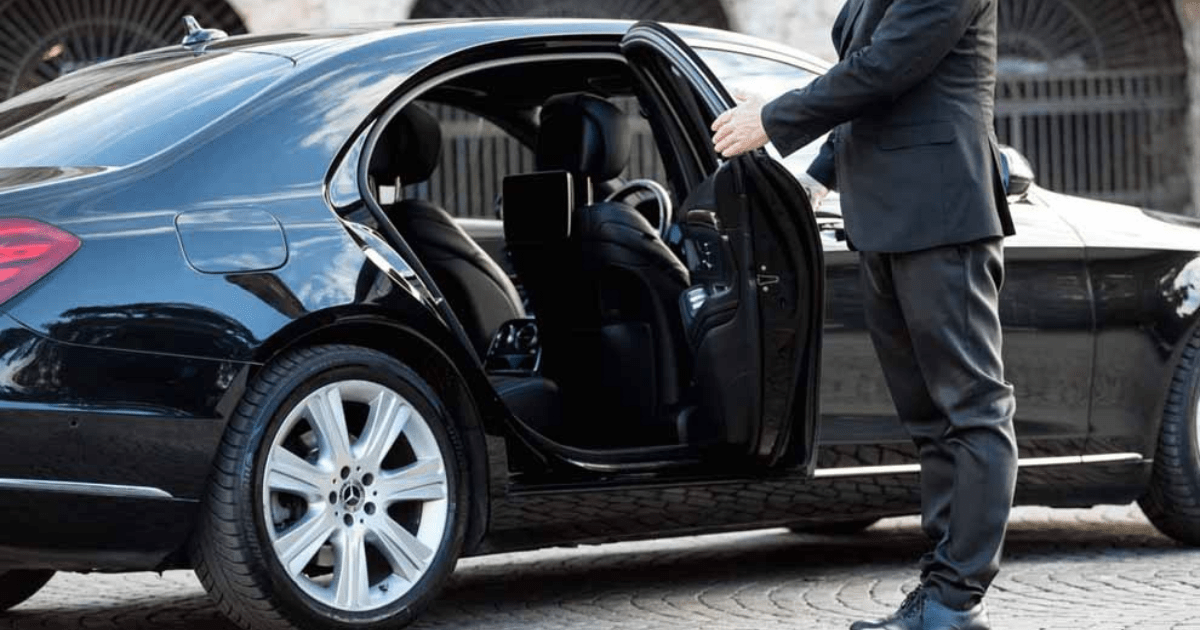 A man in a suit is opening the door of a black car.