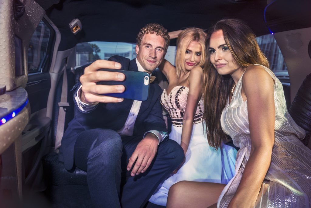 A man is taking a selfie with two women in a limousine.