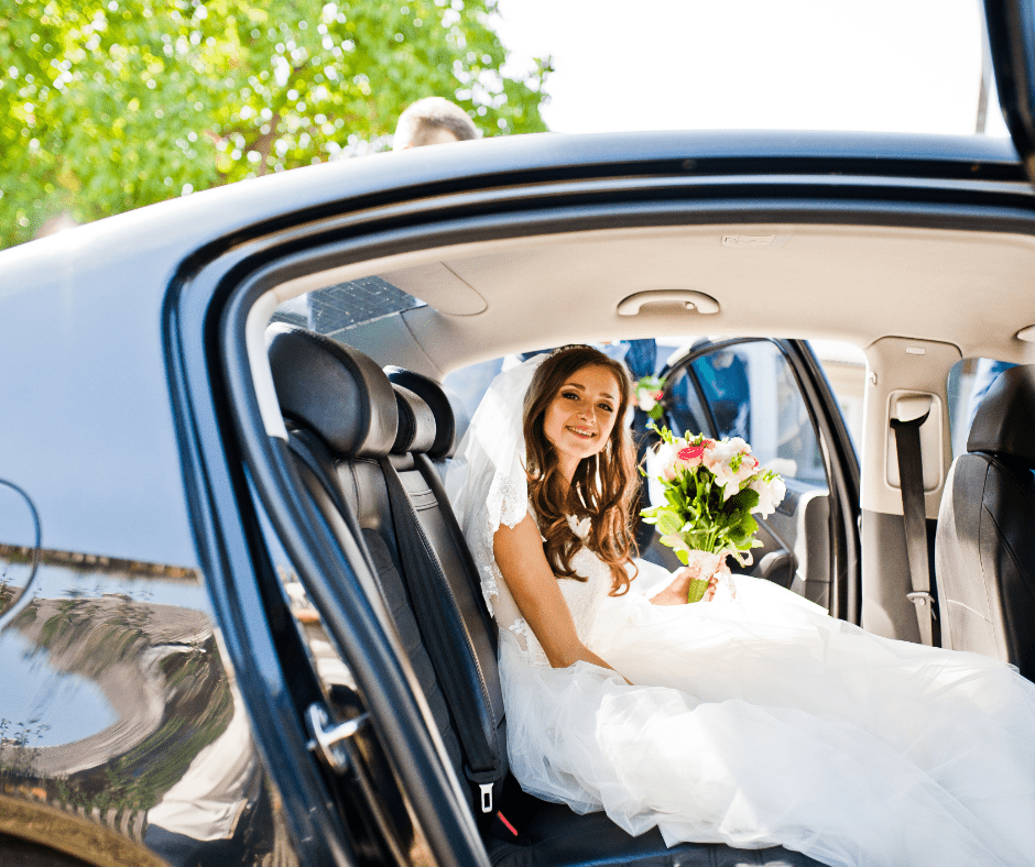 A bride is sitting in the back seat of a car holding a bouquet of flowers.