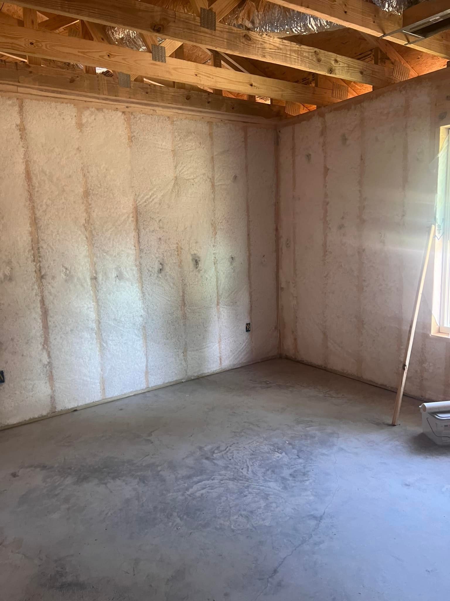 Empty room with unfinished concrete walls and floor. Exposed wooden beams are visible on the ceiling.