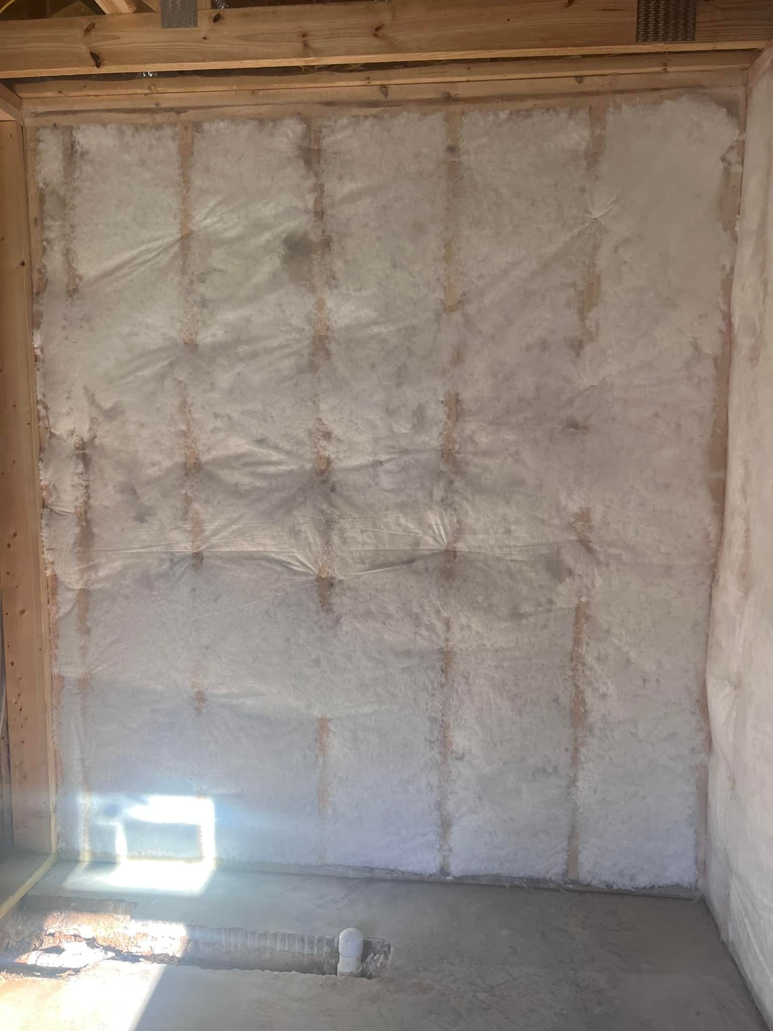 Interior wall in a building under construction, with insulation between wooden studs. Concrete floor and a vent are visible.