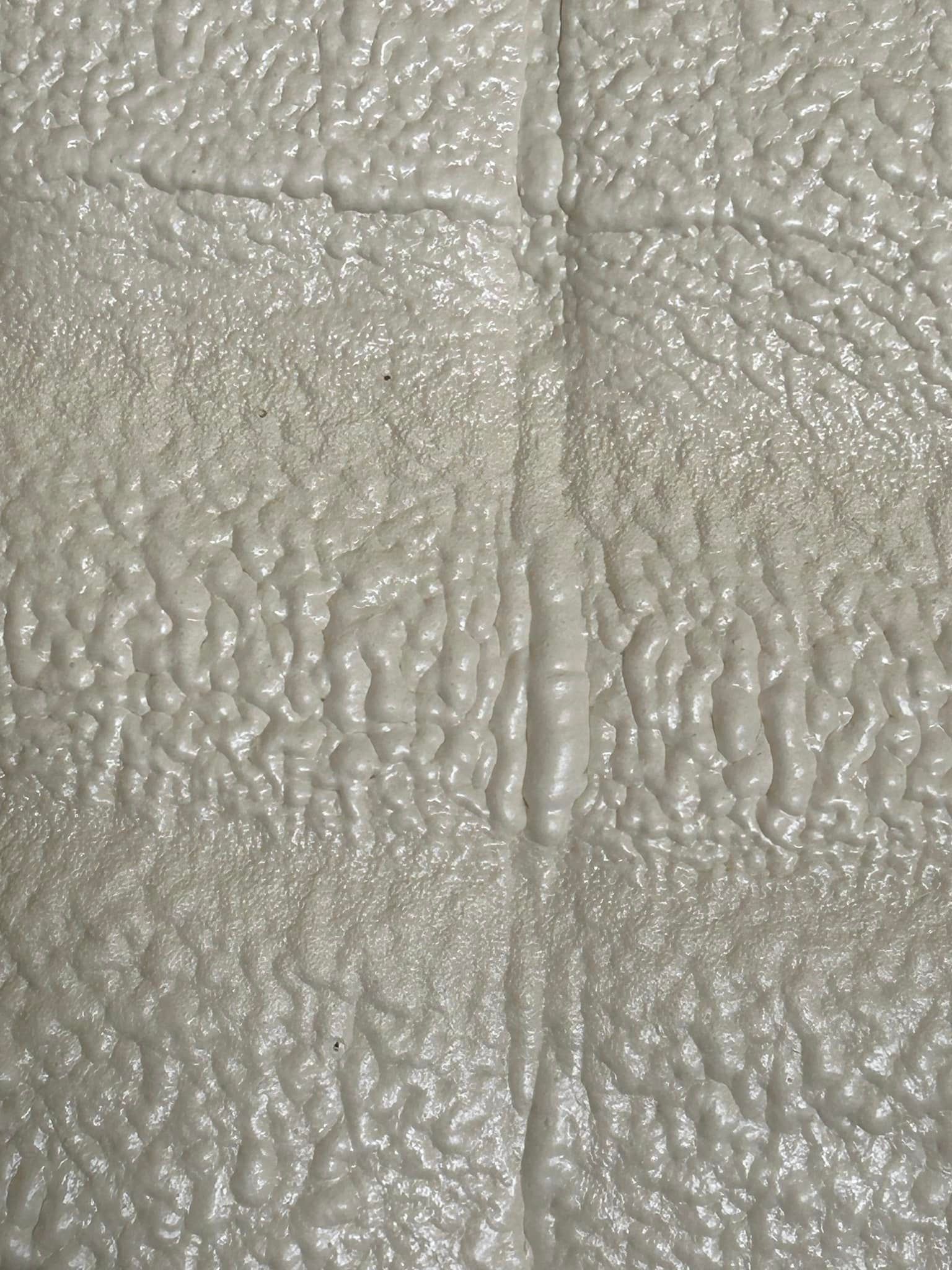 Light gray, textured surface with grid-like creases. The surface appears to be covered in tiny bubbles or bumps.