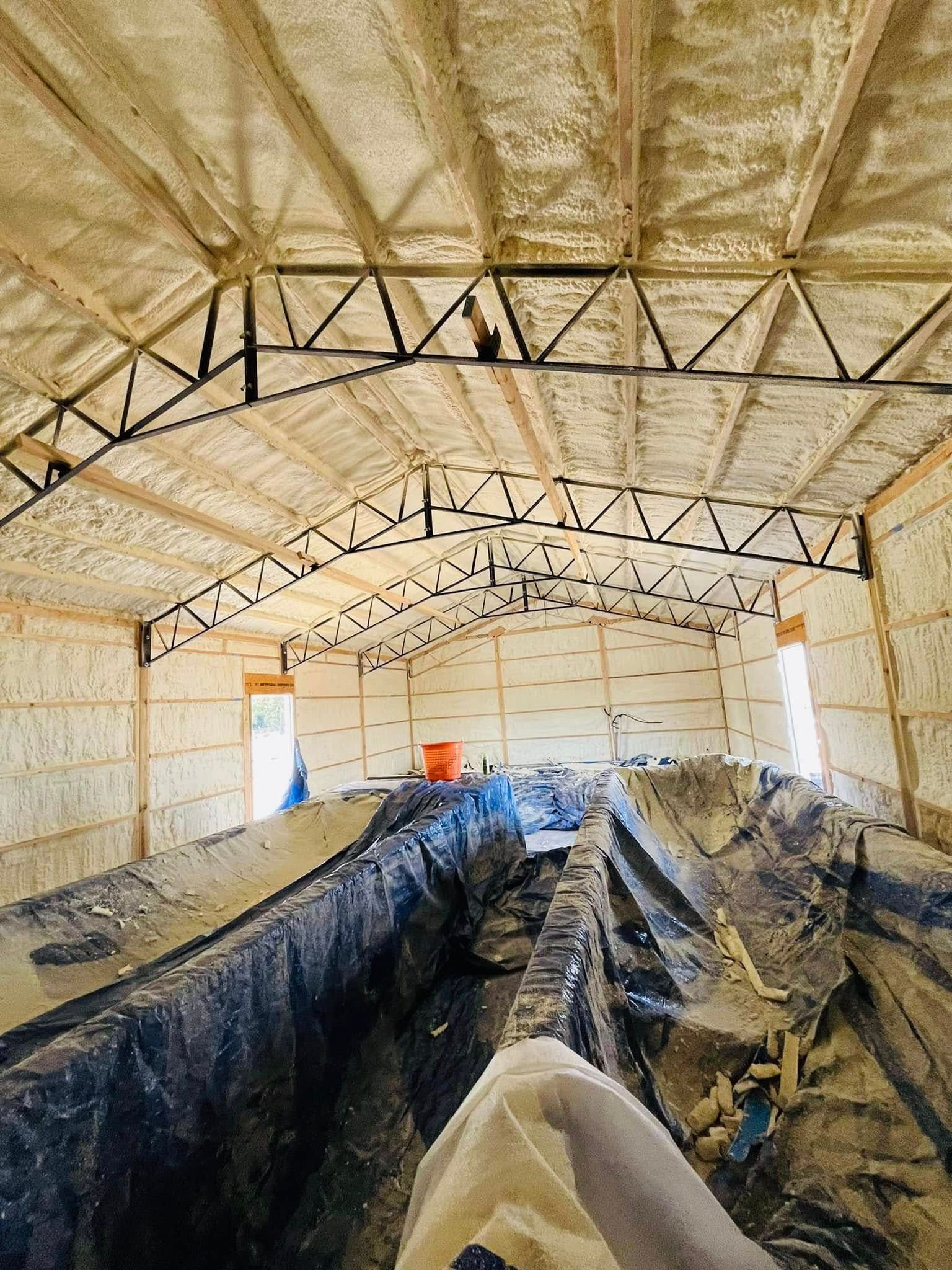 Interior of a building with spray foam insulation on walls and ceiling, exposed metal trusses. A covered pit runs the length of the floor.