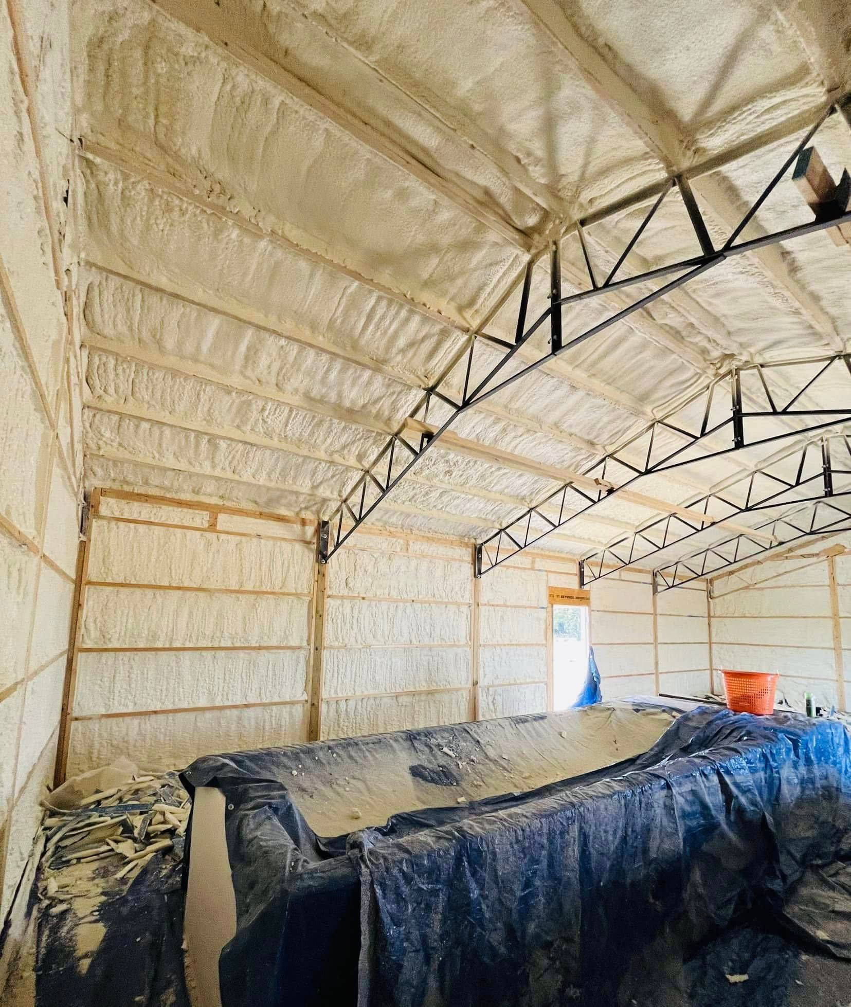 Interior view of a building with spray foam insulation on the walls and ceiling. Wooden framing supports the structure.