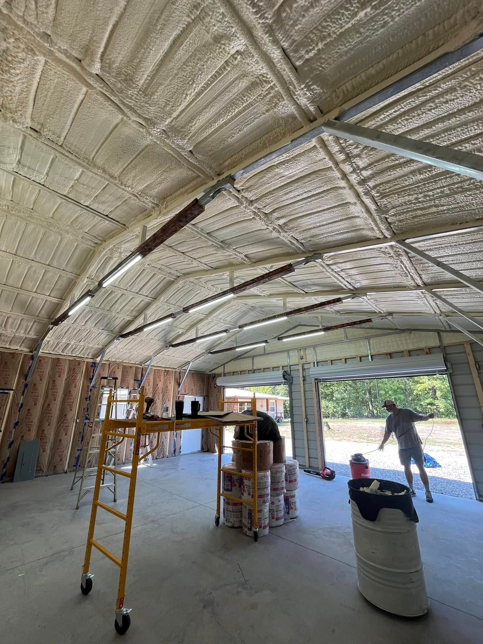 Interior of a building under construction, showing spray foam insulation on the metal roof. Workers are present with tools and supplies.