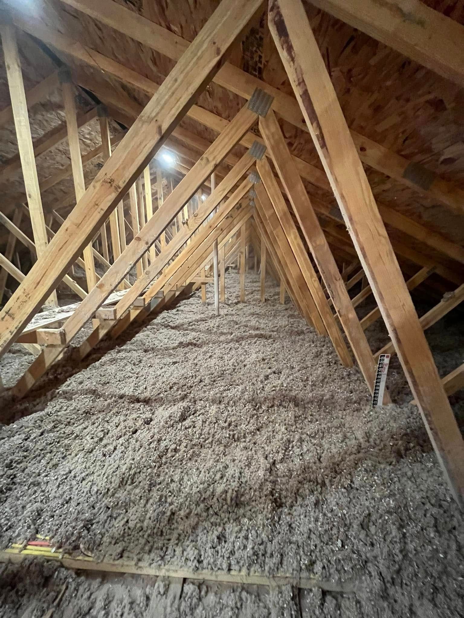 Interior view of an attic with wooden rafters and cellulose insulation. The space is long and narrow with the insulation filling the floor.