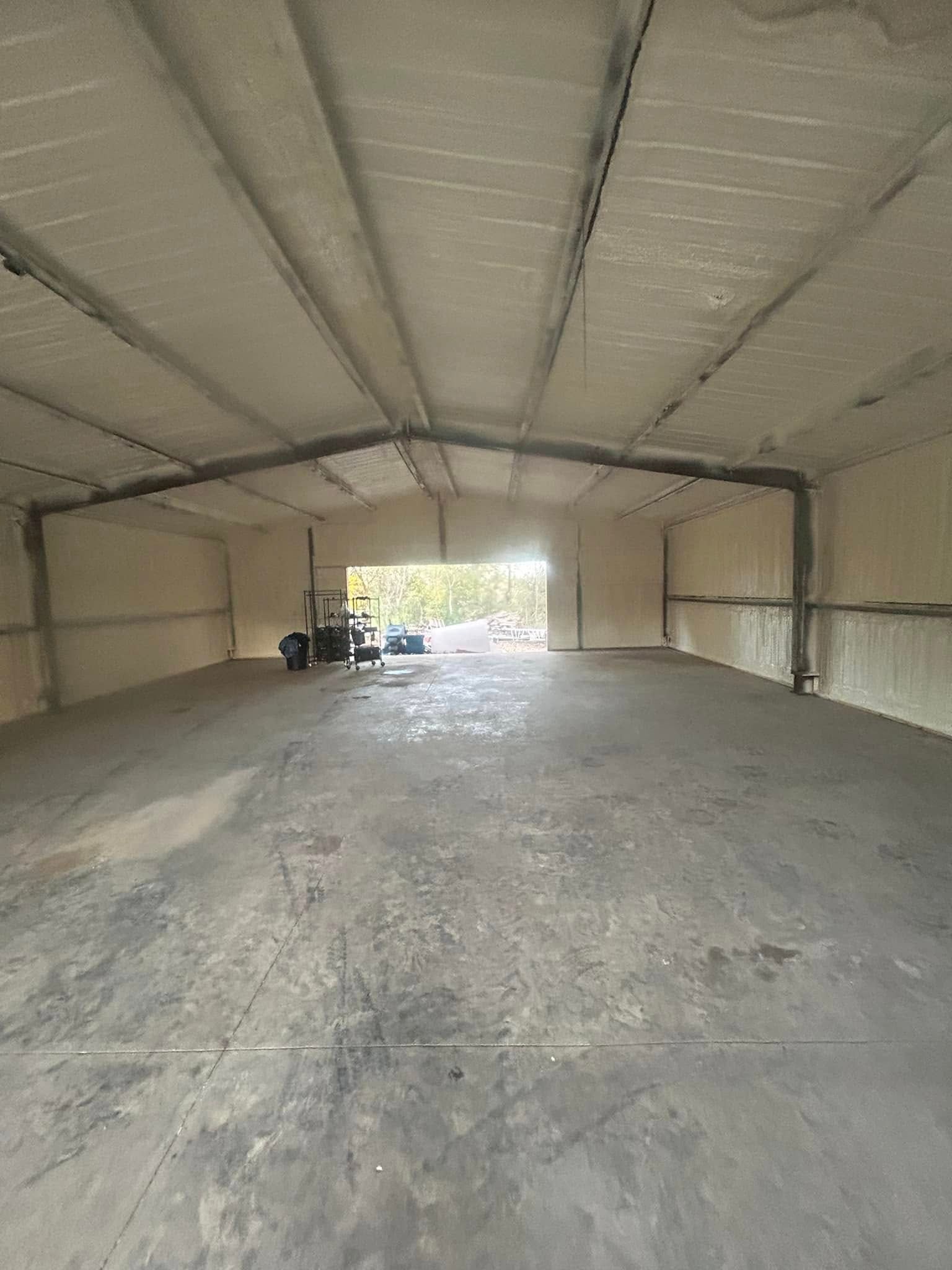 Interior of a large, empty metal building with spray foam insulation on walls and ceiling. A door provides a view to the outside.