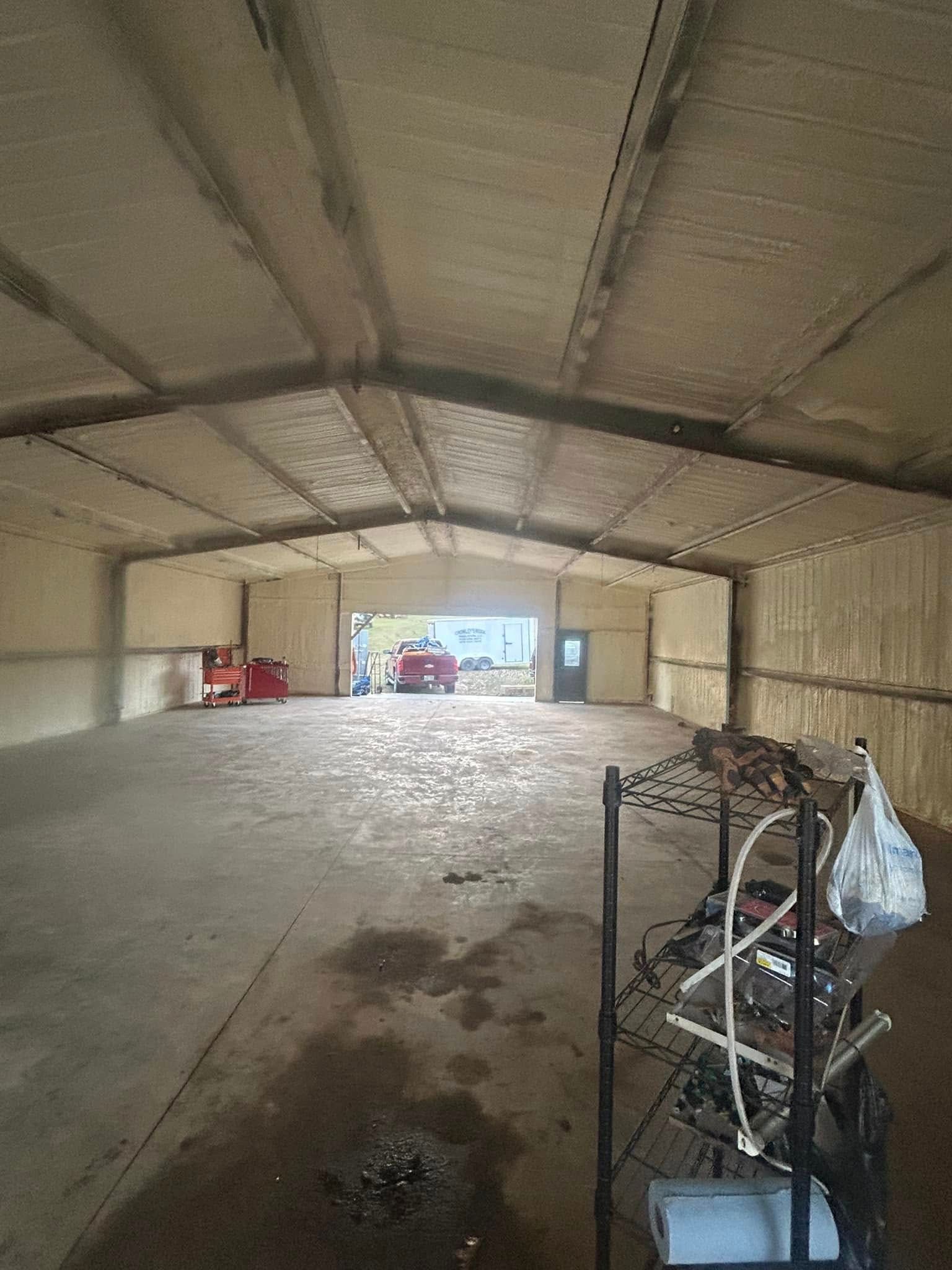 Inside a large, empty warehouse, concrete floor, light tan foam insulation on walls and ceiling. A red car is visible in the doorway.