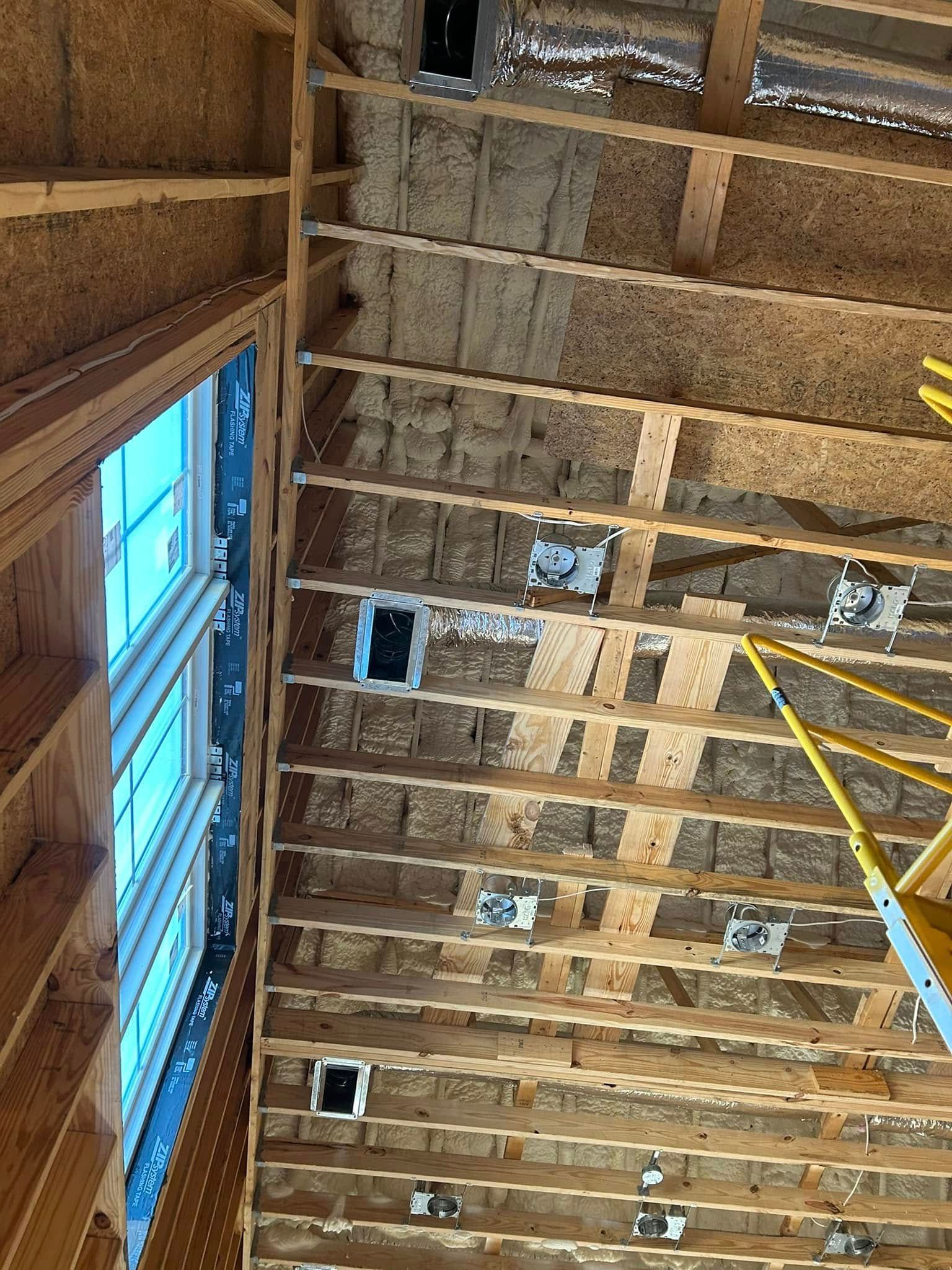 Interior view of a wood-framed roof under construction. There are electrical boxes and a window in the frame.