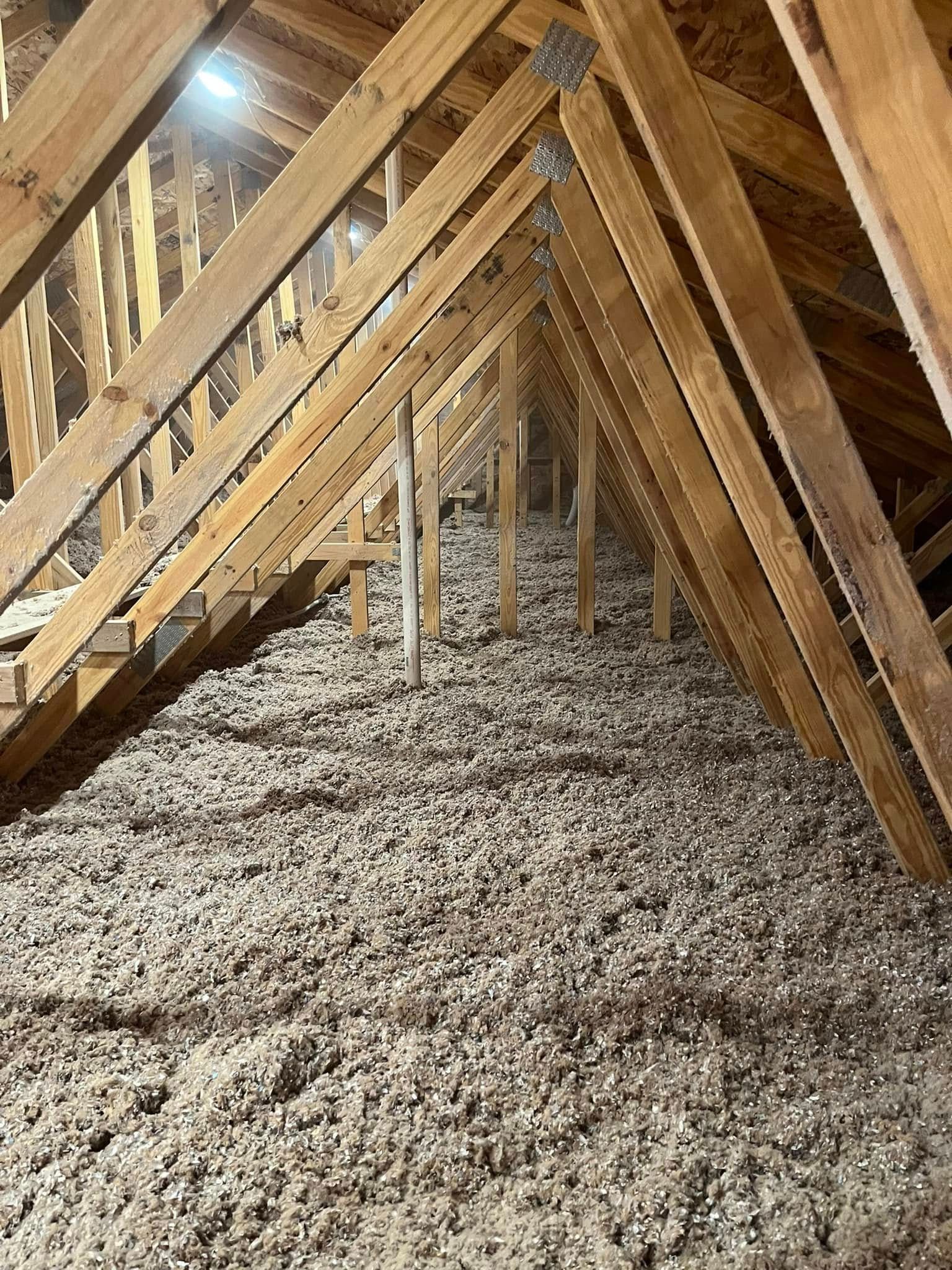 An attic filled with loose-fill insulation between wooden rafters. The beams create a triangular pattern.