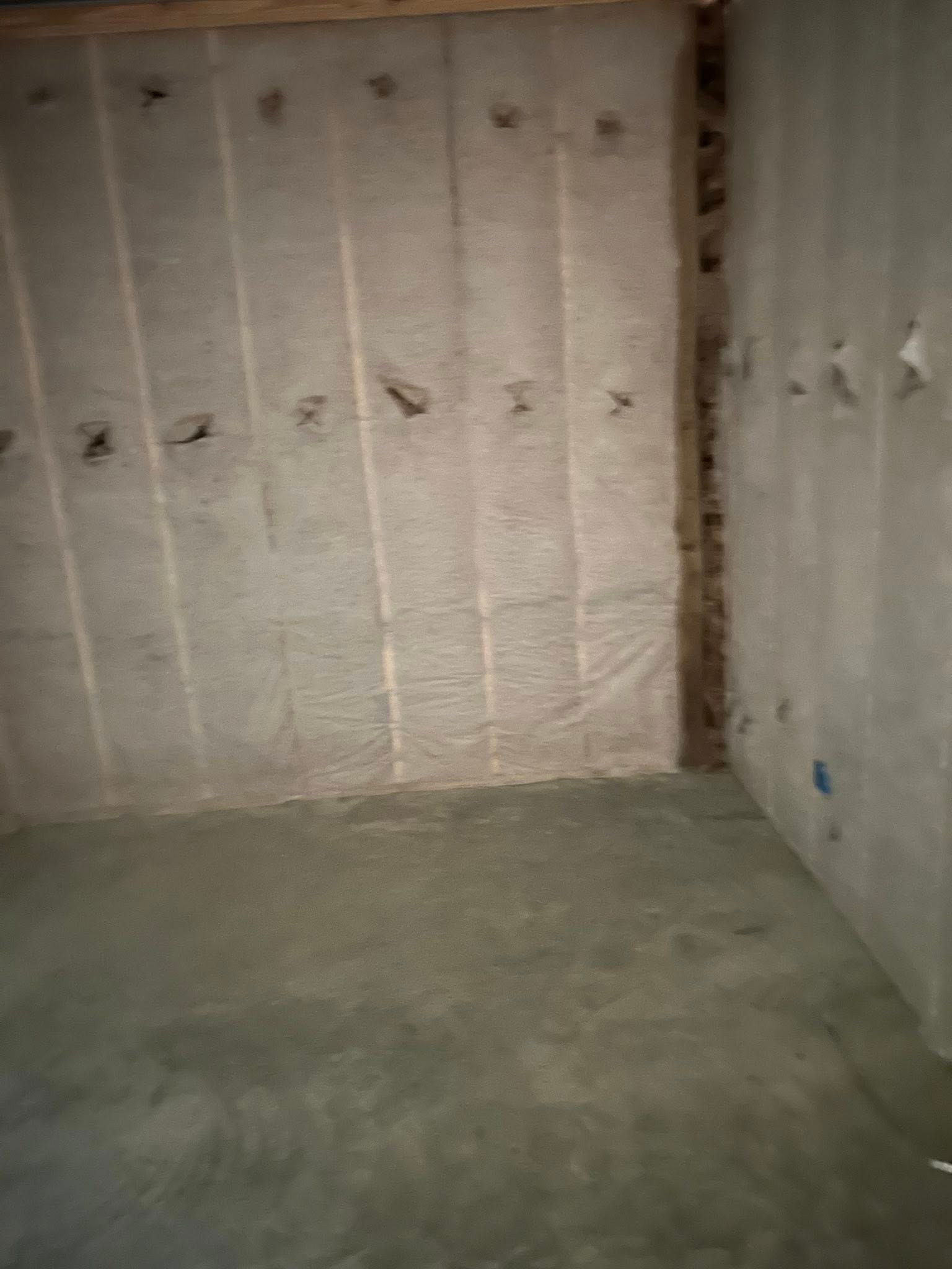 Empty room with exposed insulation between wooden studs on the walls and a concrete floor.