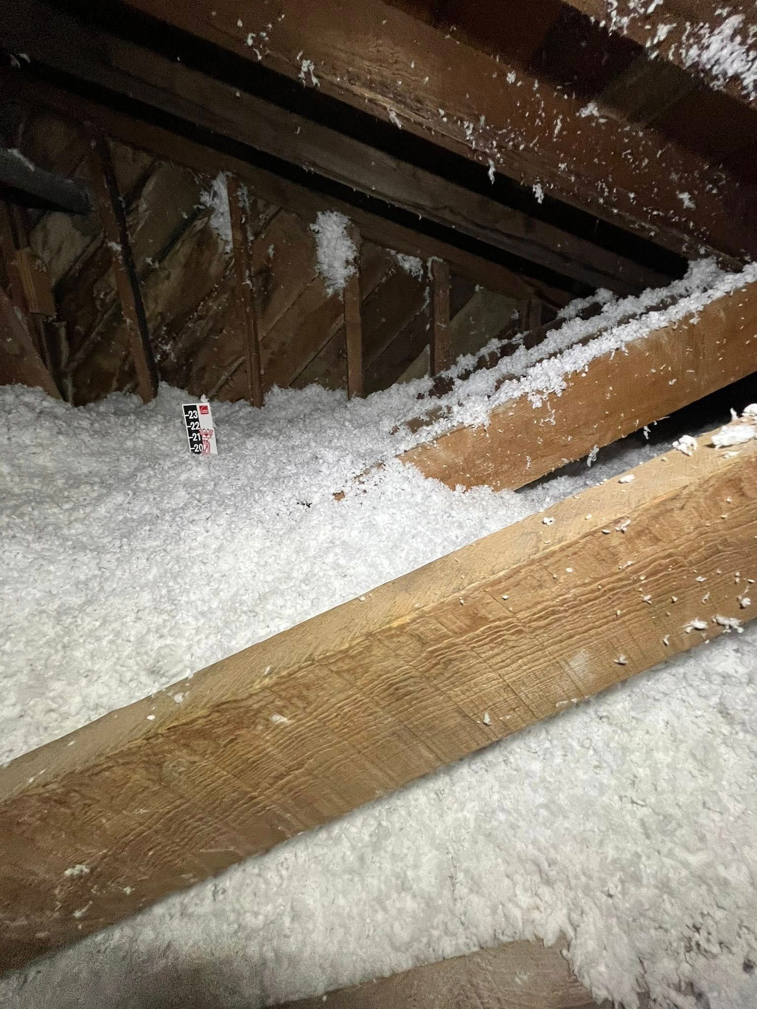 Attic with insulation covering the floor and rafters. The scene is lit, with white insulation against brown wood.