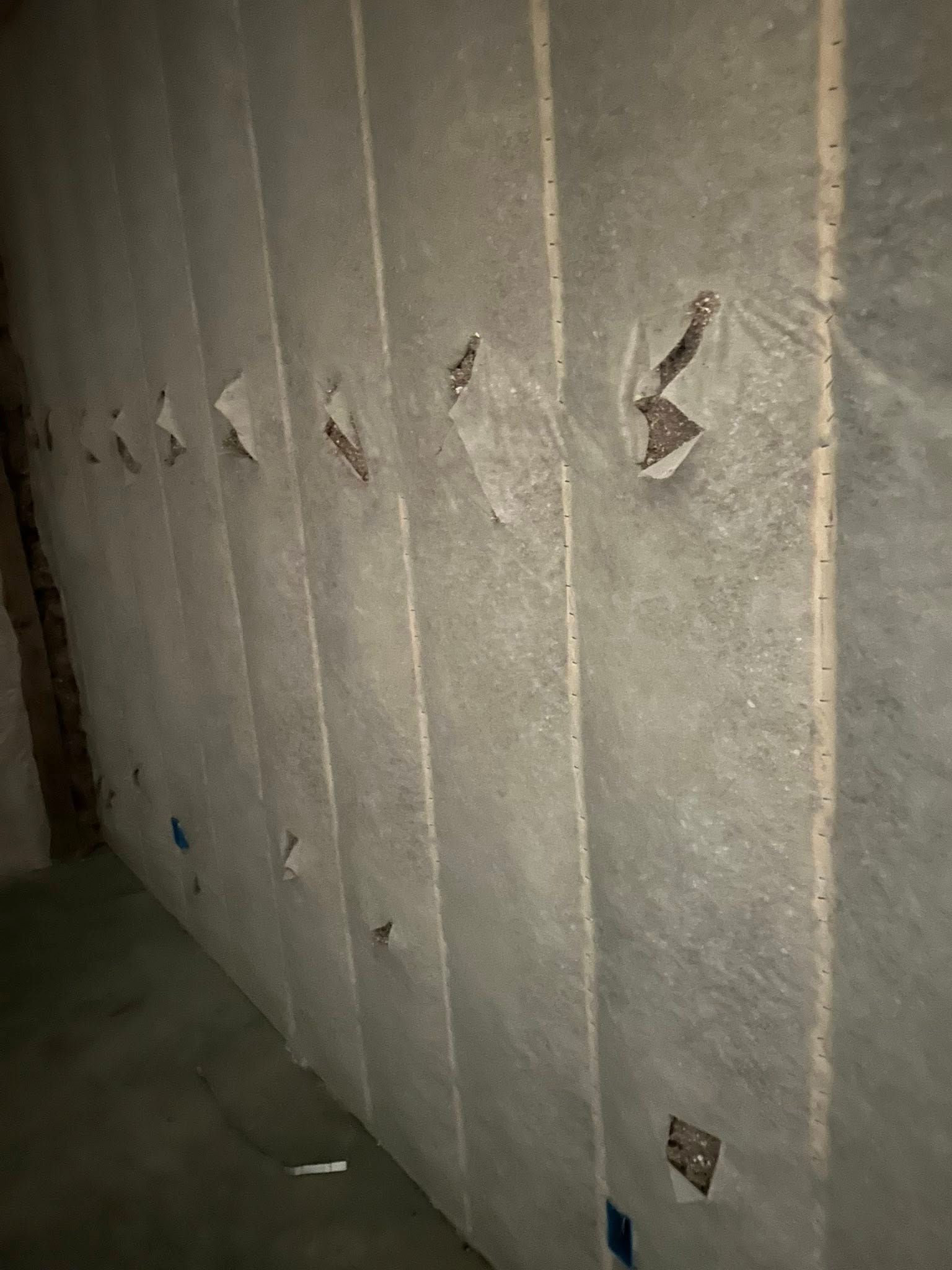 A dark interior wall with vertical lines of insulation, some torn, and exposed electrical outlets.