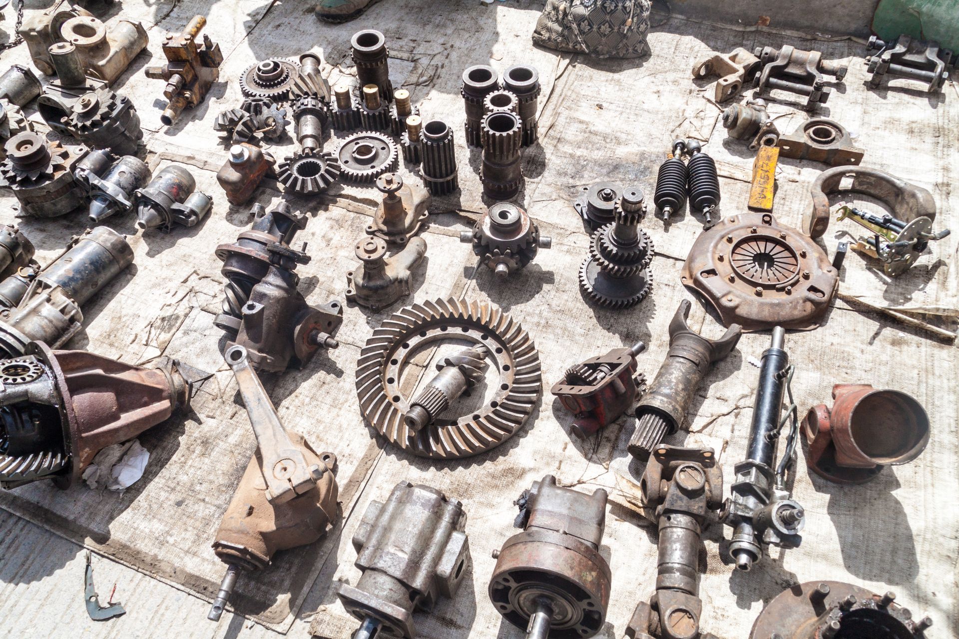 Assorted used auto parts laid out on the ground, including gears, shafts, and engine components.