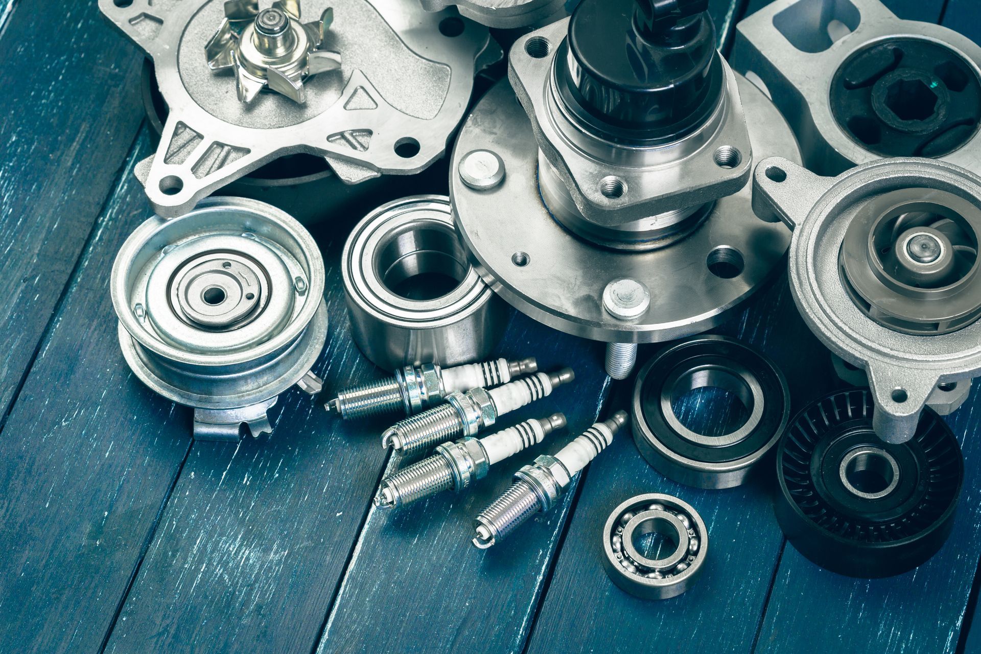 Assorted used automotive parts including spark plugs and bearings on a blue wooden background.