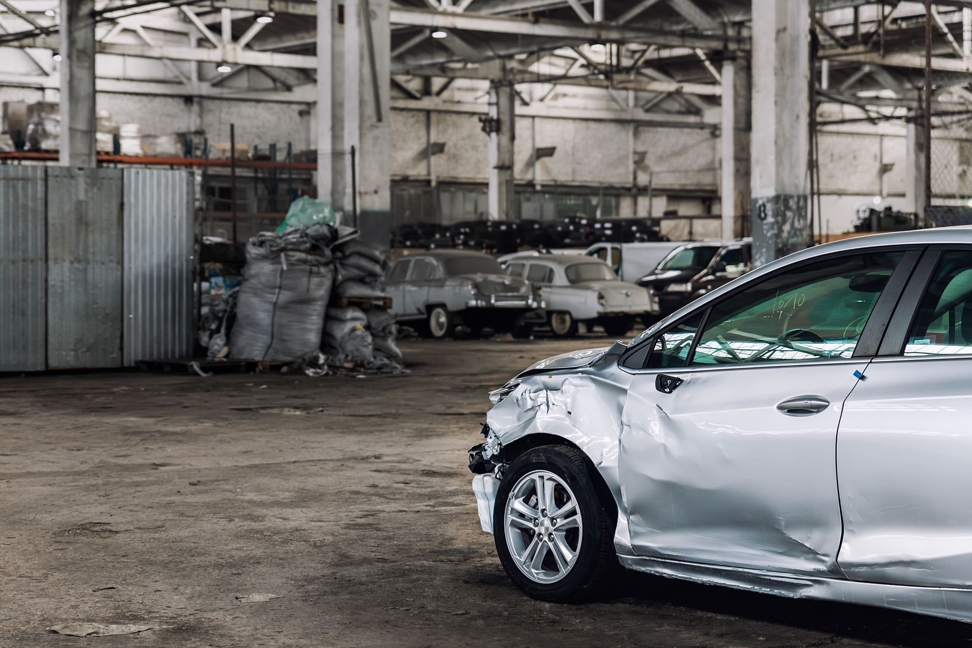 A damaged silver car with a dented rear quarter panel is parked inside a salvage warehouse A damaged silver car with a dented rear quarter panel is parked inside a salvage warehouse