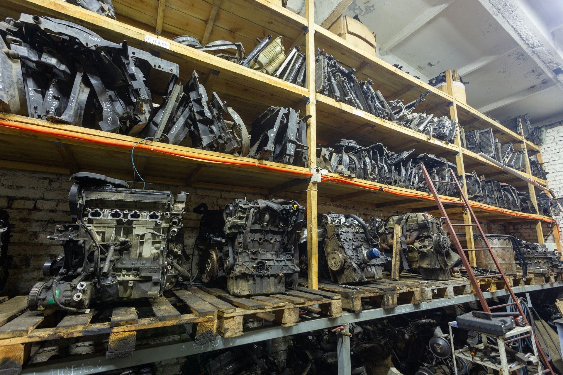 A warehouse interior featuring rows of car engines and parts stacked on wooden pallets and metal shelving units.